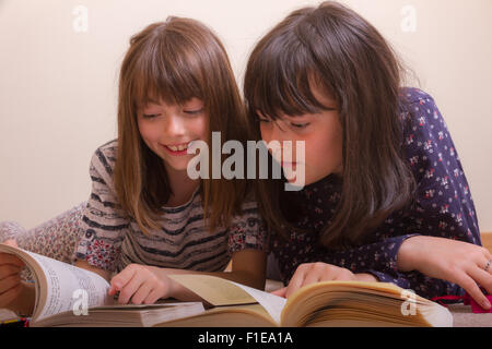 2 junge weiße 9 & 11 Jahre alte Mädchen auf dem Boden, die Bücher zu lesen, als ein Lächeln und verweist auf etwas lustiges in Ihr Stockfoto