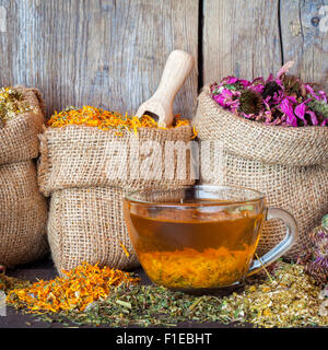 Heilkräuter in Hessischen Taschen und gesunde Teetasse auf rustikalen hölzernen Hintergrund, Kräutermedizin. Stockfoto