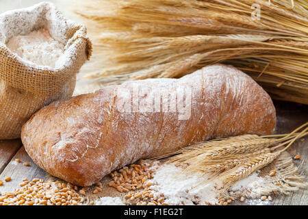 Frisches Brot, Sack Mehl und Weizen Ohren auf Holztisch. Stockfoto