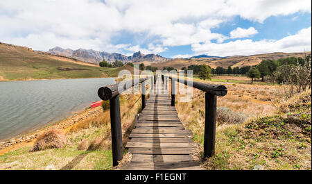 Blick durch Steg mit roten Boot am Seeufer und Drakensberg Berge in der Ferne Stockfoto