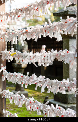 Blick entlang des Rahmens Arbeiten mit Strings ausgestreckt und viele Japanische omikuji, manchmal auch als "O-mikuji Pech fortune Papiere, Streifen, auf gebunden. Stockfoto