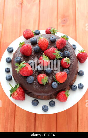 Nahaufnahme von Schokoladenkuchen mit Beeren an der Spitze aus Holz Hintergrund Stockfoto