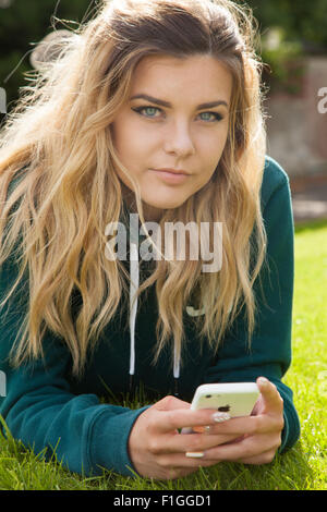 Ziemlich junges Mädchen liegend auf dem Rasen ein Mobiltelefon in ihren Händen hält. Stockfoto