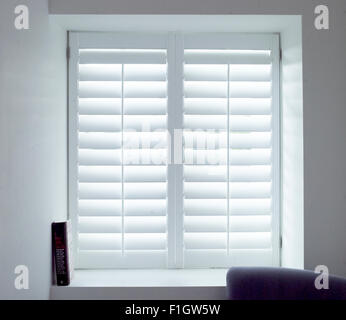 Natürliches Licht durch ein Fenster mit Fensterläden in einem weißen Raum. Stockfoto