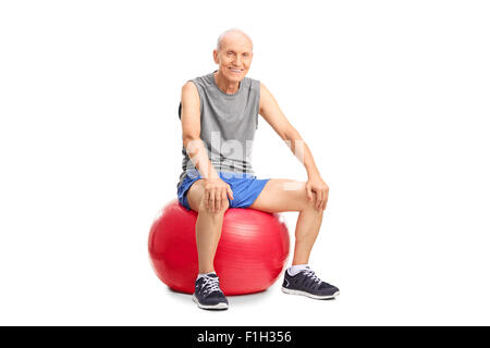 Fröhlichen senior woman Sportswear auf eine rote Fitnessball sitzen und schaut in die Kamera, die isoliert auf weißem Hintergrund Stockfoto