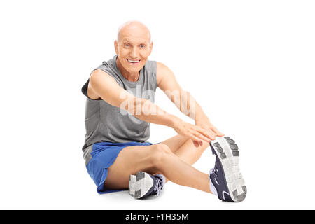 Studioaufnahme eines Senior Sportswear Dehnung Bein sitzen auf dem Boden isoliert auf weißem Hintergrund Stockfoto