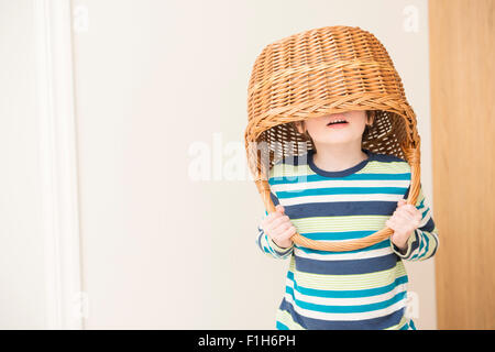 Kleine Mädchen spielen und Weidenkorb über ihren Kopf halten. Konzeptbild von Kindheit Spaß, Fantasie und Vorstellungskraft. Stockfoto