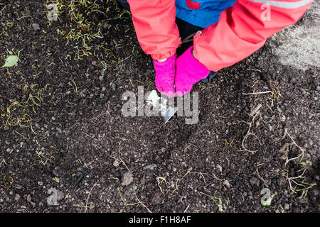 Lifestyle-Frühjahr-Szene. Kleines Mädchen Graben in die Gartenerde Vorbereitung für Blumen, Pflanzen und Gemüse. Stockfoto