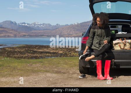 Mitte Erwachsene Frau sitzen auf Kofferraum anziehen Schuhe, Loch Eishort, Isle Of Skye, Hebriden, Schottland Stockfoto