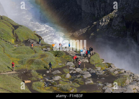 Touristen, die ins Netz gehen und den Dettifoss Wasserfall mit einem Regenbogen hinter sich im Nebel, Vatnajökull Nationalpark, Nordost Island, betrachten Stockfoto