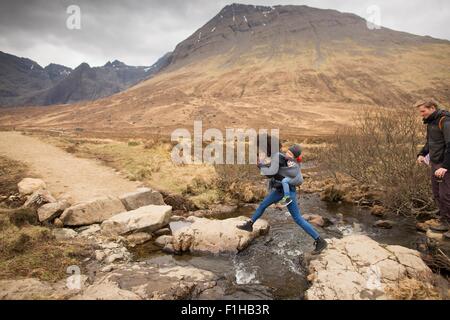 Frau springt über Bach, Fairy Pools, in der Nähe von Glenbrittle, Isle Of Skye, Hebriden, Schottland Stockfoto