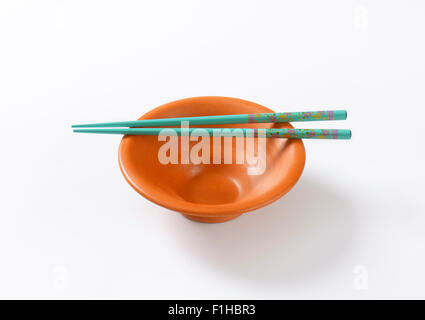 paar blaue Stäbchen und leer orange Schüssel auf weißem Hintergrund Stockfoto