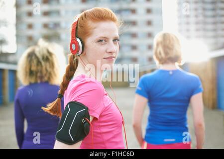 Porträt Frau mit Armbinde und Kopfhörer vor dem Training über die Schulter in die Kamera schaut Stockfoto