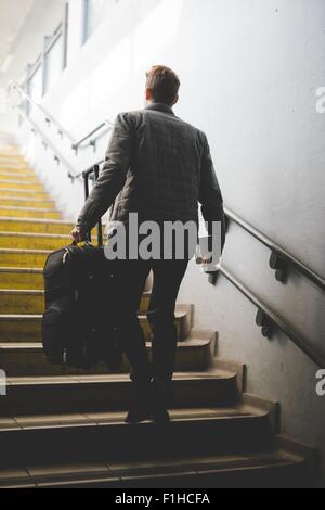 Rückansicht der junge Geschäftsmann Pendler auf Treppe, die Koffer zu tragen. Stockfoto