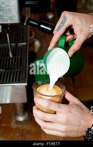 Hände des Café Kellner gießt Milchschaum in Latte Glas Stockfoto