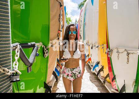 Porträt der jungen Frau, die zwischen Surfbretter mit Bikini, Strand von Waikiki, Oahu, Hawaii, USA Stockfoto