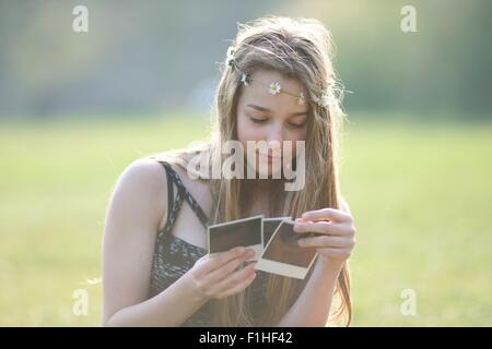 Teenager-Mädchen tragen Daisy-Chain Kopfschmuck Blick auf sofortige Fotos im park Stockfoto