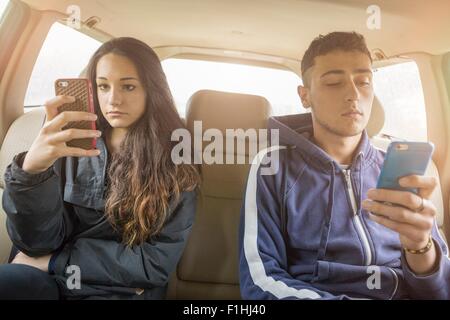 Teenager-Mädchen und jungen Mann liest eigene Smartphone Texte auf dem Auto Rücksitz Stockfoto