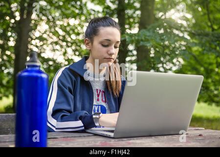 Junges Mädchen im Park mit Laptop bei Picknickbank Stockfoto