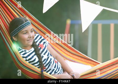 Porträt von niedlichen Mädchen mit Haarband und Zopf im gestreiften Garten Hängematte liegend Stockfoto