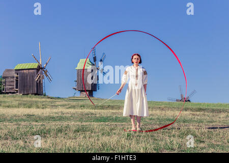 Mädchen in ethnische Tracht gekleidet steht auf einem Feld Hintergrund mit Windmühlen Stockfoto