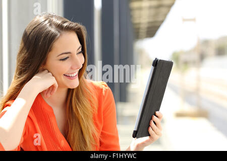 Glückliche Frau liest ein Tablet oder e-Book in einem Bahnhof und wartet für den öffentlichen Verkehr Stockfoto