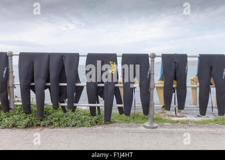 Acht Neoprenanzüge drapiert über eine Schiene am Straßenrand in Sennen Cove, Cornwall, eine bekannte Surfen und Wassersport. UK Stockfoto