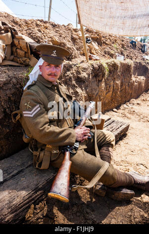 Weltkrieg ein Re-enactment, Britische Graben 1914, mit Soldat, Unteroffizier sitzen mit Gewehr auf dem Schoß, Kopf drehte sich um Zuschauer zu suchen. Stockfoto