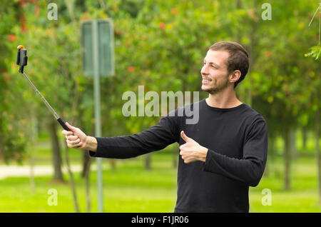 Hispanic Mann posiert mit Selfie Stick in Park Umgebung lächelnd Stockfoto