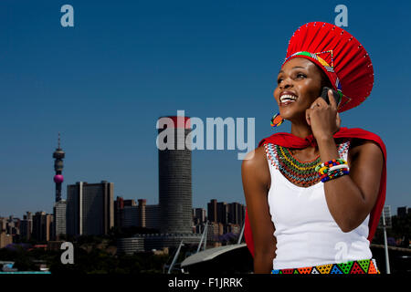 Traditionell gekleidete Afrikanerin Gespräche über Handy mit Stadtansicht im Hintergrund Stockfoto