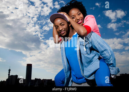 Junge schwarze Frau auf die Schultern des Mannes vor Stadtbild Stockfoto