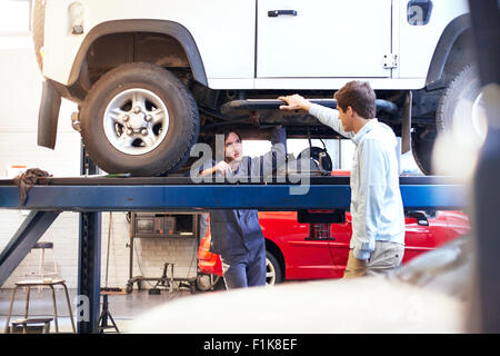 Mechaniker unter Auto im Gespräch mit Kunden im Auto-Werkstatt Stockfoto