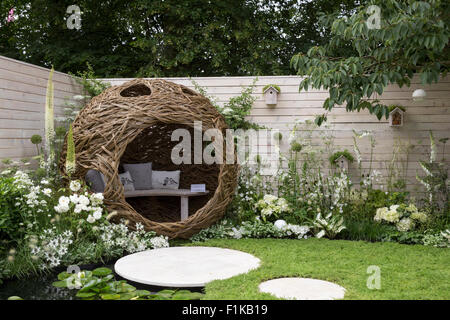 Eine kleine städtische Tierwelt Vogel freundlich Garten Kamille Rasen Schritt Steine und eine gewebte Weidenschote mit Bank und Kissen - weiße Blumen Sommer UK Stockfoto