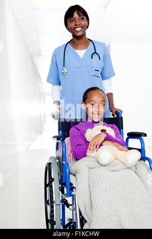 Ein Arzt, eine Mädchen mit einem Teddy im Rollstuhl schieben Stockfoto