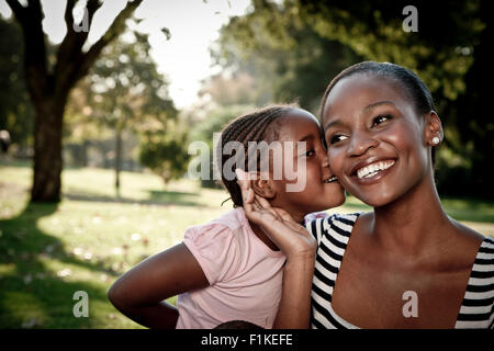 Junge afrikanische Mädchen küssen ihre Mutter auf die Wange in einem park Stockfoto