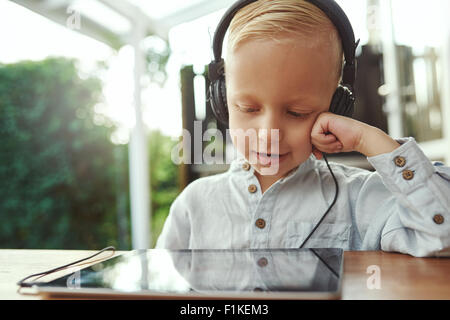 Entzückende junge sitzt mit einem Tabletcomputer hören seine Musik-Bibliothek mit einem glücklichen Lächeln der Zufriedenheit auf einer Reihe von s Stockfoto