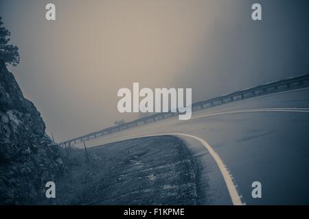 Nebligen geschwungene Straße. Gefährliche Bergstraße. Bläuliche Color-Grading. Stockfoto