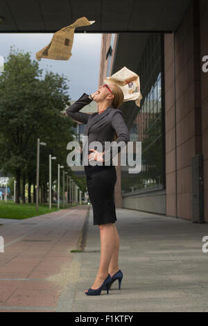 Junge blonde Geschäftsfrau mit einer fliegenden Zeitung über den Kopf in der Stadt. Stockfoto