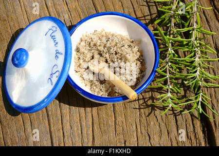 Kleine Porzellanschale mit Fleur de Sel und einem Zweig Rosmarin auf einem rustikalen Holztisch Stockfoto