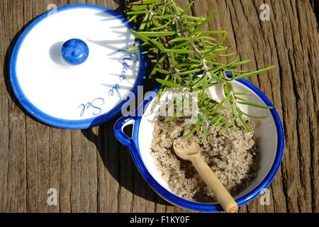 Kleine Porzellanschale mit Fleur de Sel und einem Zweig Rosmarin auf einem rustikalen Holztisch Stockfoto