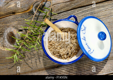 Kleine Porzellanschale mit Fleur de Sel und einem Zweig Rosmarin auf einem rustikalen Holztisch Stockfoto