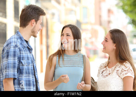 Drei glückliche Freunde sprechen, wobei ein Gespräch auf der Straße an einem sonnigen Tag mit Gebäuden im Hintergrund Stockfoto