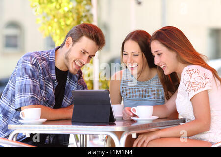 Drei glückliche Freunde Fernsehen oder soziale Medien in einer Tablette in einer Café-Terrasse Stockfoto