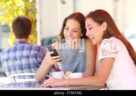 Zwei glückliche Freunde oder Schwestern teilen ein Smartphone in einer Café-Terrasse Blick auf Gerät im Sommer Stockfoto