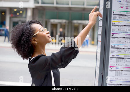 junge Frau, die Überprüfung der Busfahrplan auf der Straße Stockfoto