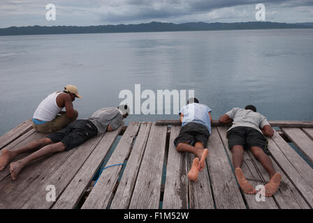 Menschen liegen auf einem hölzernen Steg und blicken auf das Meer in Arborek, einer kleinen Insel im Meeresschutzgebiet der Dampier Strait. Stockfoto