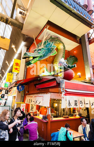 Japan, Osaka. Dotonbori, berühmten Kinryu Ramen noodle Ecke Restaurant mit Golden Dragon Abbildung Zeichen über. Die Leute draußen sitzen Diner essen. Besetzt. Stockfoto