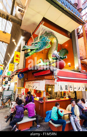 Japan, Osaka. Dotonbori, berühmten Kinryu Ramen noodle Ecke Restaurant mit Golden Dragon Abbildung Zeichen über. Die Leute draußen sitzen Diner essen. Besetzt. Stockfoto