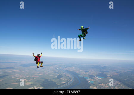 Diese Freefly-Fallschirmspringer fliegen hoch in den blauen Himmel über schöne Landschaft. Dabei fliegen sie training sitzen die Position. Stockfoto