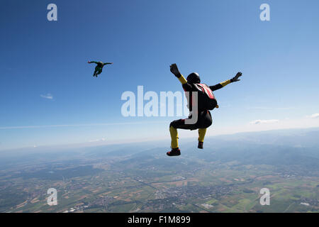 Diese Freefly-Fallschirmspringer fliegen hoch in den blauen Himmel über schöne Landschaft. Dabei fliegen sie training sitzen die Position. Stockfoto